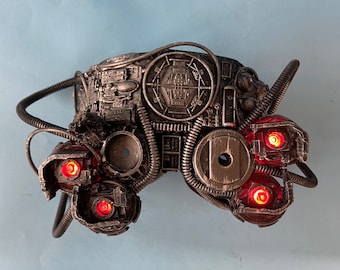 May include: A steampunk-style mask with intricate details and red LED lights. The mask is made of metal and has a circular design with gears and pipes.