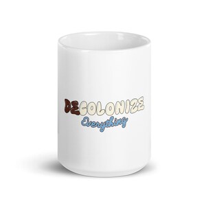 Könnte beinhalten: Weiße Keramiktasse mit dem Text "DECOLONIZE Everything" in bunten, blasenartigen Buchstaben.