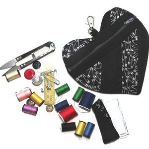 Può includere: Un kit da cucito nero a forma di cuore con cerniera, motivo a spilli bianchi e chiusura argentata. Vari accessori per cucire tra cui forbici, rocchetti di filo, bottoni, ditale e un piccolo righello.
