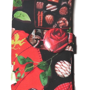 May include: A red and black fabric wallet with a rose button closure. The fabric features a pattern of chocolates, roses, and leaves.