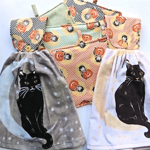 Op de afbeelding: Set van vier Halloween-thema keukendoeken. Twee handdoeken hebben een zwart kattenontwerp met een wassende maan, één handdoek heeft een zwart-wit stippenpatroon met zwarte katten en één handdoek heeft een zwart-wit stippenpatroon met oranje en zwarte pompoenen.