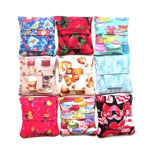 Puede incluir: Nueve pequeñas bolsas de tela cuadradas con varios diseños. Los diseños incluyen fresas, tazas de café, abejas, macarons y corazones. Las bolsas son en tonos de azul, rojo, rosa y beige. Cada bolsa tiene un cierre de solapa.