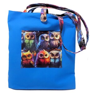 May include: A bright blue tote bag with a colorful owl design. The bag features a rectangular patch with six owls in various colors. The handles and a button closure have a patterned design.