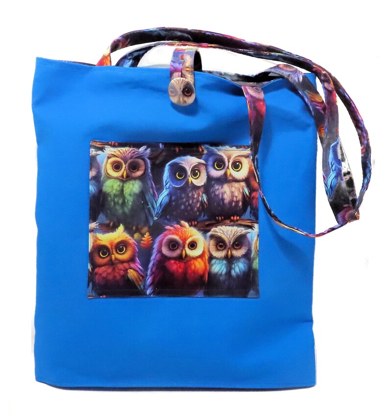 May include: A bright blue tote bag with a colorful owl design. The bag features a rectangular patch with six owls in various colors. The handles and a button closure have a patterned design.