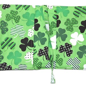 May include: Green fabric book cover with a shamrock pattern in various shades of green, black, and white. The cover has two handles and a tie closure. The shamrocks have polka dots, stripes, and checkered patterns.