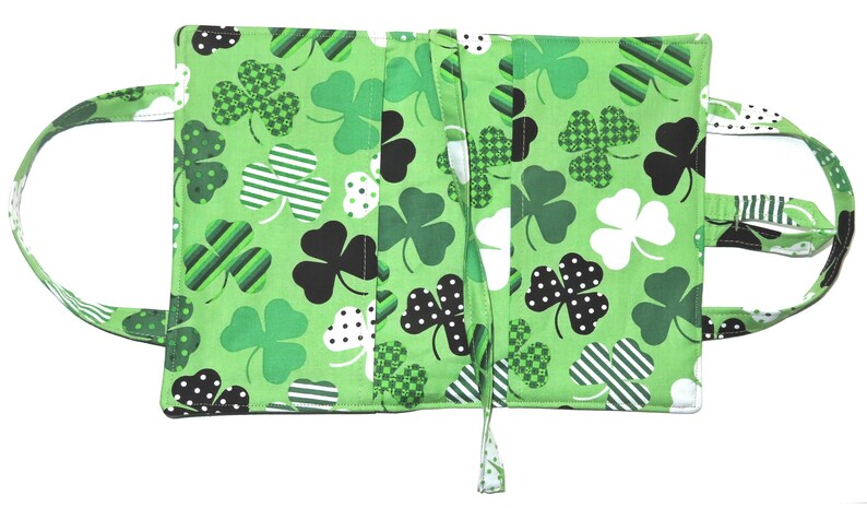 May include: Green fabric book cover with a shamrock pattern in various shades of green, black, and white. The cover has two handles and a tie closure. The shamrocks have polka dots, stripes, and checkered patterns.