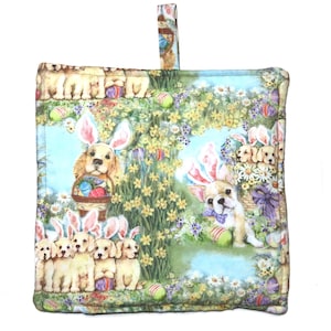 May include: Square quilted pot holder with a colorful Easter-themed design. The fabric features illustrations of puppies wearing bunny ears, surrounded by Easter eggs and flowers. A loop is attached for hanging.