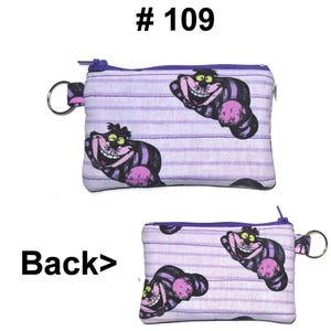 May include: Two small, rectangular coin purses with a purple zipper and key ring. The purses feature a repeating pattern of the Cheshire Cat from Alice in Wonderland on a light purple striped background. The text "# 109" is at the top.