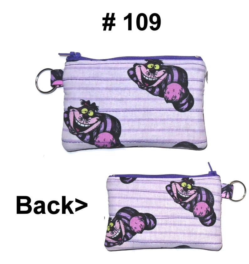 May include: Two small, rectangular coin purses with a purple zipper and key ring. The purses feature a repeating pattern of the Cheshire Cat from Alice in Wonderland on a light purple striped background. The text "# 109" is at the top.