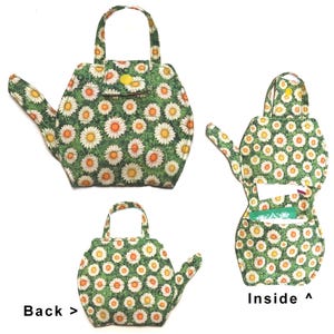 May include: A fabric teapot-shaped purse with a green background and a daisy pattern. The purse has a handle, a small flap with a yellow button, and a spout. The inside of the purse is visible, showing a pocket.