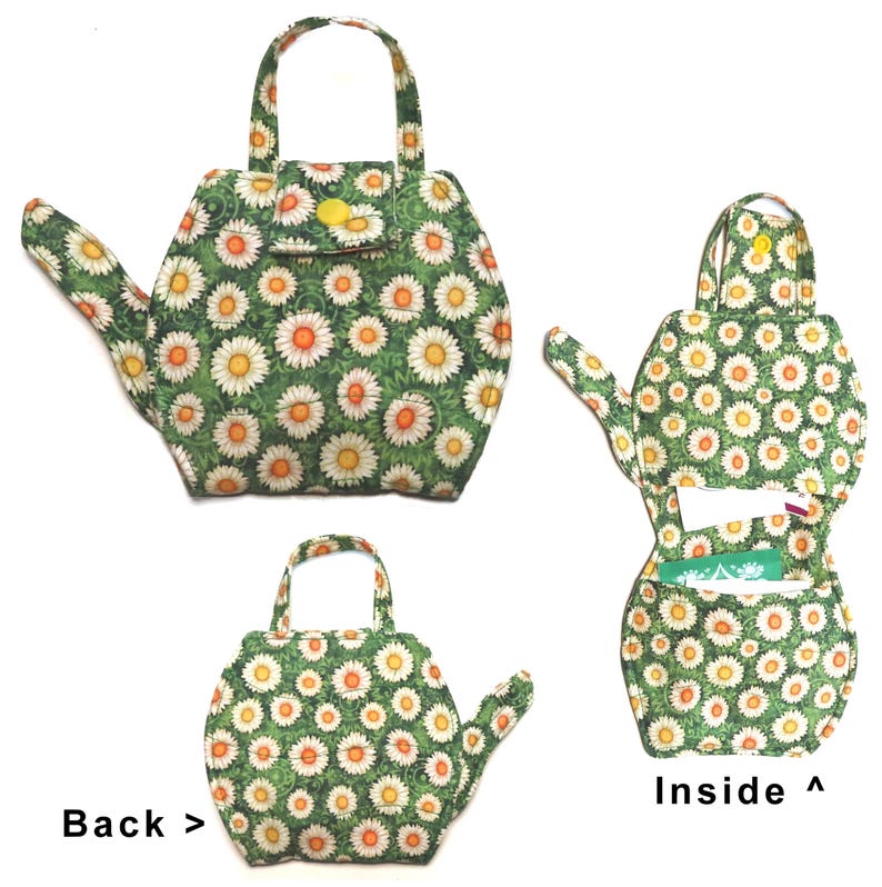 May include: A fabric teapot-shaped purse with a green background and a daisy pattern. The purse has a handle, a small flap with a yellow button, and a spout. The inside of the purse is visible, showing a pocket.