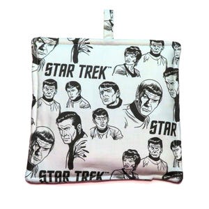 May include: A white Star Trek themed pot holder featuring black and white character illustrations and the words "STAR TREK". It has a loop for hanging.