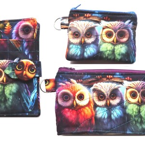 May include: A set of three owl-themed accessories: a wallet with a pen, a small coin purse, and a larger zippered pouch. The items feature a colorful owl design with vibrant blues, greens, and reds against a dark background.