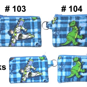 May include: Blue plaid coin purses with zipper closures and key rings. One purse features Buzz Lightyear, the other a green dinosaur. The text "# 103" and "# 104" are printed above the purses. The word "Backs" is printed below the purses.