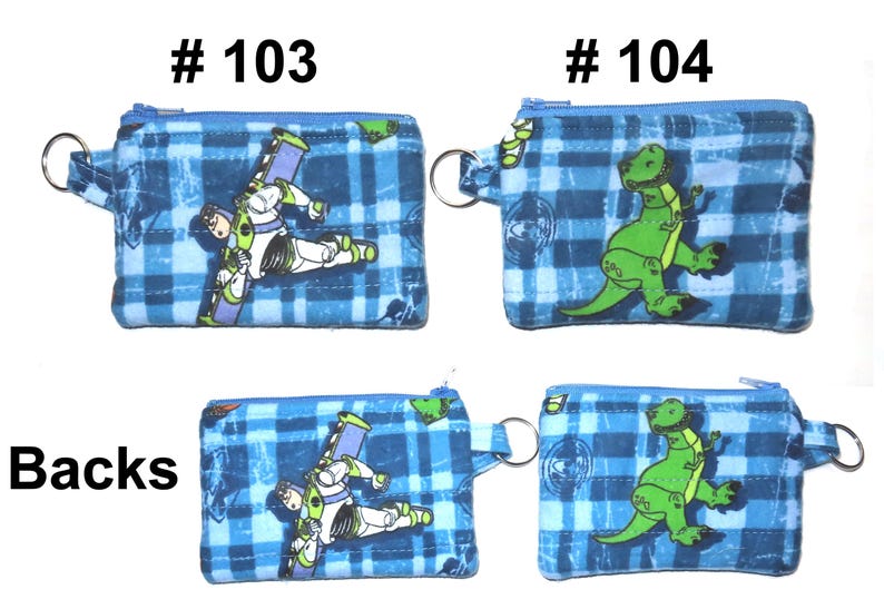 May include: Blue plaid coin purses with zipper closures and key rings. One purse features Buzz Lightyear, the other a green dinosaur. The text "# 103" and "# 104" are printed above the purses. The word "Backs" is printed below the purses.