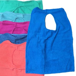 May include: A stack of colorful terry cloth bibs in shades of blue, green, pink, and orange. The bibs have a rounded neck opening and a rectangular shape, perfect for protecting clothing during meals or activities.