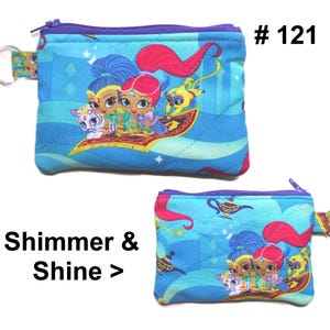 May include: Two small, blue, quilted coin purses with a zipper closure and a key ring. The purses feature a colorful graphic of characters from Shimmer and Shine. The text "Shimmer & Shine >" is printed on the image.