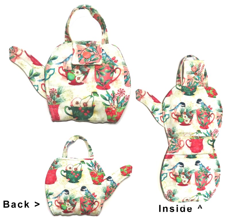 May include: A fabric teapot-shaped tea cozy with a handle and spout. The cozy is cream-colored and covered in a pattern of red teacups, pears, and birds. The back of the cozy is visible, along with the inside, showing the same pattern.