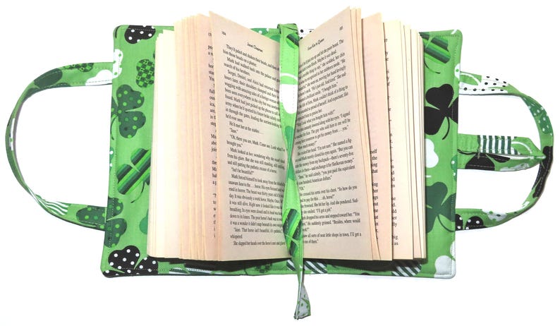 May include: A green book cover with a St. Patrick's Day theme, featuring shamrocks and white polka dots. The cover has handles and a matching bookmark. The book is open, revealing the pages.