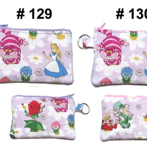 May include: Four small, rectangular coin purses with zipper closures and key rings. The purses feature illustrations from Alice in Wonderland, including the Cheshire Cat, Alice, and other characters, set against a floral background. The text "# 129" and "# 130" is visible.