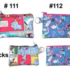 May include: Four small, rectangular coin purses with zippers and key rings. Two purses feature a Dumbo the Elephant comic strip design, and two feature Eeyore from Winnie the Pooh. The purses have a variety of colors, including red, blue, and pink.