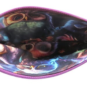 May include: A purple zippered pouch with a vibrant owl print interior. The pouch features a key ring attachment and a contrasting purple zipper. The owl design includes shades of blue, purple, and brown.