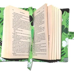 May include: Open book with a green shamrock-patterned cover and bookmark. The cover features various shamrock designs in white, black, and green. The bookmark is a matching green with a shamrock pattern. The book is open to reveal text.