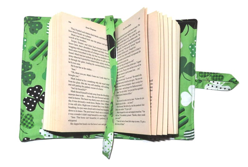 May include: Open book with a green shamrock-patterned cover and bookmark. The cover features various shamrock designs in white, black, and green. The bookmark is a matching green with a shamrock pattern. The book is open to reveal text.