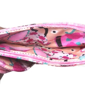 May include: A folded, pink fabric wallet with a colorful interior. The interior features a pattern of pink, peach, and teal abstract shapes. The exterior is a solid pink with a black border.