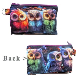 May include: Quilted zippered pouch featuring a vibrant owl design. The pouch showcases three owls in shades of red, blue, and green, with a purple zipper and a small loop on the side. The back of the pouch also features the owl design.