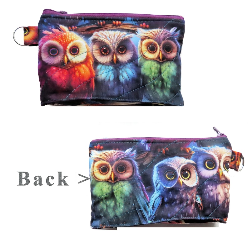 May include: Quilted zippered pouch featuring a vibrant owl design. The pouch showcases three owls in shades of red, blue, and green, with a purple zipper and a small loop on the side. The back of the pouch also features the owl design.