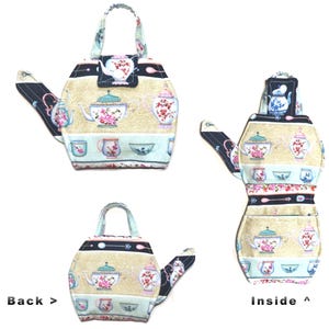 May include: A fabric teapot-shaped tea cozy with a handle. The cozy features a beige background with floral teapots, cups, and bowls. The spout and handle are navy blue with a white floral pattern. The cozy is designed to keep tea warm.