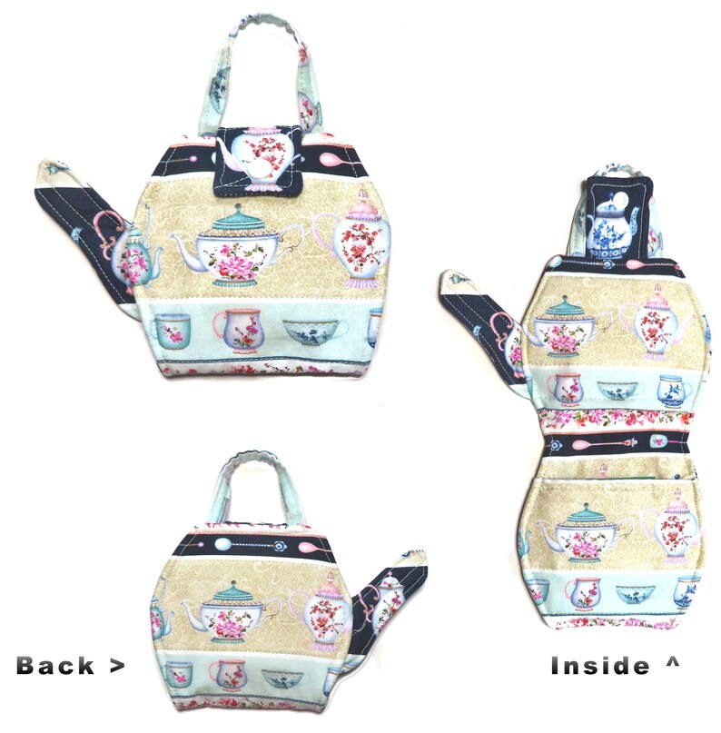 May include: A fabric teapot-shaped tea cozy with a handle. The cozy features a beige background with floral teapots, cups, and bowls. The spout and handle are navy blue with a white floral pattern. The cozy is designed to keep tea warm.