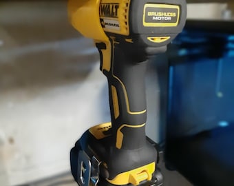May include: A yellow and black cordless drill with a brushless motor. The drill is hanging from a metal surface by a magnetic hook. The drill has a battery attached to it.