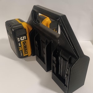 Może przedstawiać: Czarny plastikowy uchwyt na baterie z uchwytem. Uchwyt ma trzy gniazda na baterie. W jednym z gniazd znajduje się bateria DeWalt 5Ah 18V XR Li-Ion w kolorze żółtym i czarnym.