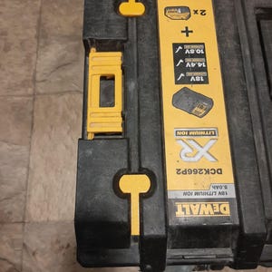 Può includere: Una cassetta degli attrezzi DeWalt nera e gialla con la scritta "DEWALT 18V LITHIUM ION 5.0Ah DCK266P2 XR LITHIUM ION" stampata sul davanti. La cassetta ha due chiusure gialle sulla parte superiore e una maniglia gialla sul lato.