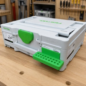 Pode incluir: Uma mala de armazenamento Festool Systainer cinza-claro com um fecho frontal verde brilhante e um suporte de acessórios verde correspondente fixado na frente. A mala apresenta o logótipo Festool no topo e na frente, com o texto systainer3.