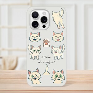 Könnte beinhalten: Hellgraue Handyhülle mit Cartoon-Illustrationen einer weißen Katze mit verschiedenen Gesichtsausdrücken. Der Text "Marie the moody cat" ist ebenfalls auf der Hülle zu sehen. Die Illustrationen umfassen einen Pfotenabdruck, das Hinterteil einer Katze und mehrere Katzen-Gesichter.