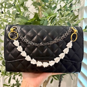 Pu&ograve; includere: Borsa nera trapuntata con tracolla a catena e dettagli floreali bianchi. La borsa presenta finiture color oro e chiusura con patta. La tracolla &egrave; una combinazione di una catena di metallo e una catena di perline bianche.
