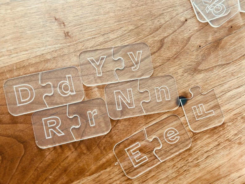 May include: Clear acrylic puzzle pieces with white engraved letters spelling out "DADDY" and "LOVE" on a wooden surface. The pieces are interlocking, creating a fun and educational toy.