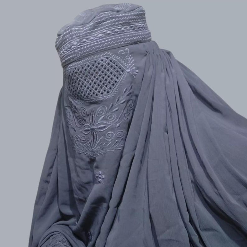 May include: A gray niqab with white embroidery. The embroidery features a geometric pattern and floral designs.
