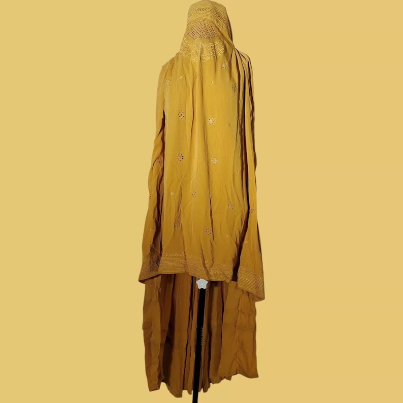 May include: A long, mustard yellow garment with a high neckline and embroidered details. The garment is made of a soft, flowing fabric and has a long, flowing skirt.