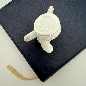 Puede incluir: Maceta de cactus de cer&aacute;mica blanca con base redonda y tres patas. La maceta est&aacute; sobre una superficie de cuero azul oscuro.