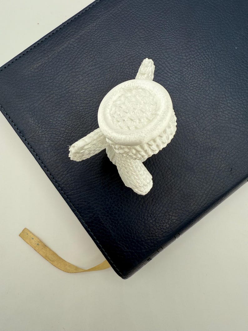 Puede incluir: Maceta de cactus de cer&aacute;mica blanca con base redonda y tres patas. La maceta est&aacute; sobre una superficie de cuero azul oscuro.