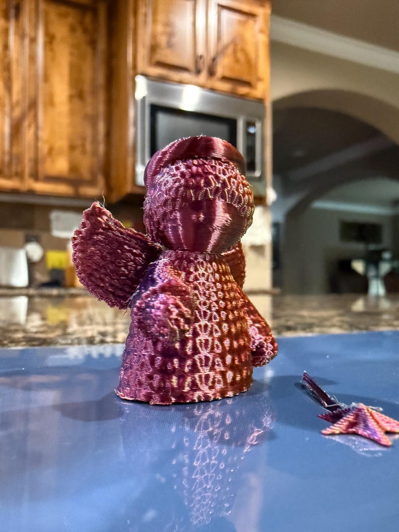 Puede incluir: Una figurita de &aacute;ngel impresa en 3D con un degradado de color rosa y morado. El &aacute;ngel tiene un dise&ntilde;o detallado con una superficie texturizada. A la figurita le falta un ala.