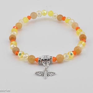 May include: A yellow, orange, and clear crystal beaded bracelet with a silver butterfly charm. The bracelet is made with round beads and has a silver toggle clasp.