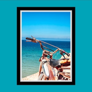 Peut inclure: Une moto vintage rouillée garée sur une plage de sable surplombant une mer bleue. La moto a une selle en cuir marron et un réservoir d'essence chromé.