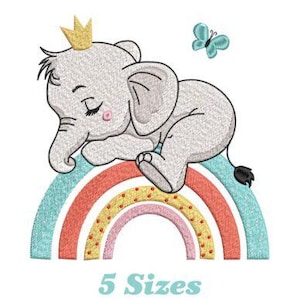 Puede incluir: Diseño bordado de un elefante gris con una corona dorada, durmiendo sobre un arcoíris con una mariposa azul arriba. El arcoíris tiene rayas rojas, naranjas, amarillas y azules con lunares blancos.