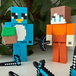 May include: Two block-style figures, one blue and one orange, with pixelated accessories. The blue figure holds a block of grass and dirt. Several pixelated swords and pickaxes are scattered around the figures. The figures and accessories are made of plastic.