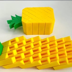 May include: Two yellow and green pineapple shaped objects made of plastic. The larger pineapple is a cube and the smaller pineapple is a long, curved shape.